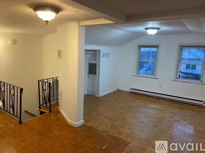 A room with wooden flooring and white walls, with a window showing a snowy scene outside.