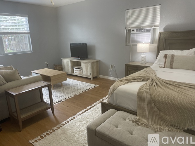 A bedroom with a bed, a couch, a chair, a TV, and a window.
