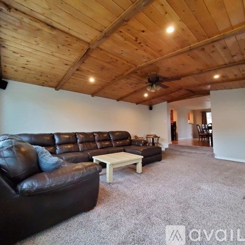 A living room with a brown leather couch and a wooden ceiling.