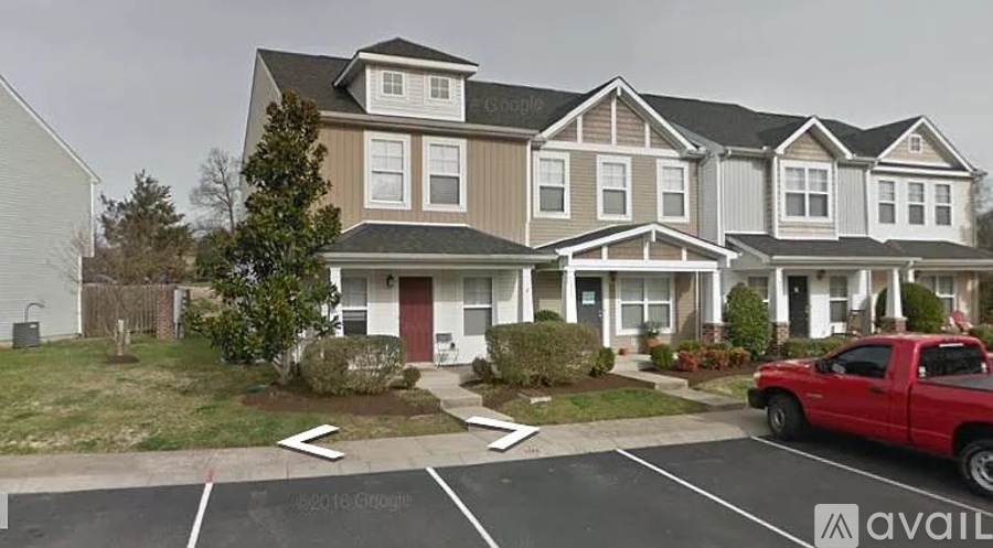 A red truck is parked in a parking lot in front of a two-story house.