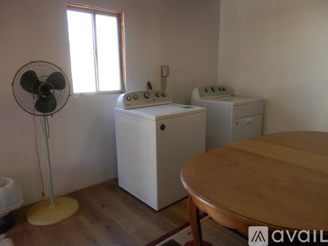 A room with a fan, a table, and two white appliances.