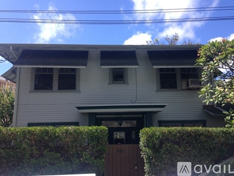 A house with a white facade and a brown door is surrounded by a green hedge.