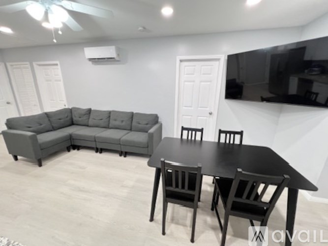 A living room with a grey sofa, black table and chairs, and a flat-screen TV mounted on the wall.
