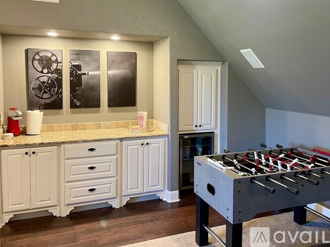 A foosball table is in the middle of a kitchen with white cabinets and a countertop.