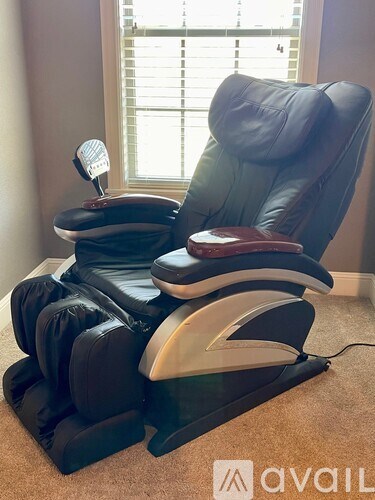 A black massage chair with a red cushion and a white headrest is in front of a window.
