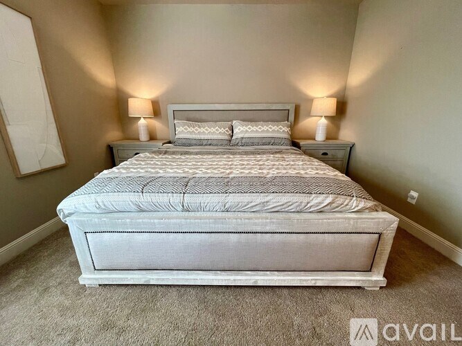 A bed with a white comforter and two pillows sits in a room with two wall lamps.