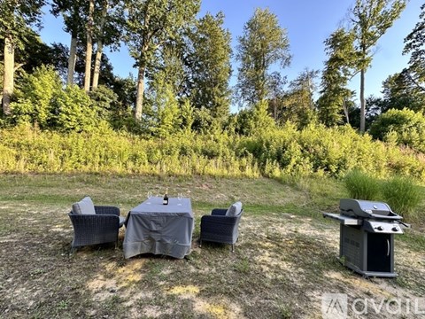 A table with chairs and a grill set up in a grassy area with trees in the background.
