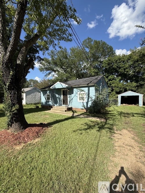 A blue house with a white house in the background and a tree in front of the house.