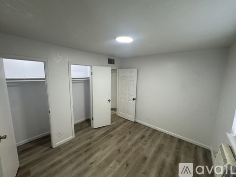 A room with white walls and wooden flooring, with a window on the left side.