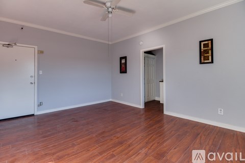A room with wooden floors and white walls, with a ceiling fan and two doors.