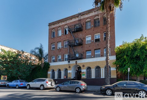 A street view of a multi-story building with cars parked in front.