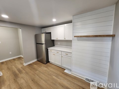 A kitchen with white cabinets and a wooden shelf is available.