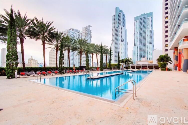 A pool surrounded by palm trees and lounge chairs with a city skyline in the background.