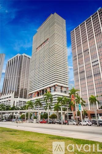 A tall building with a red sign on it stands in front of other buildings.