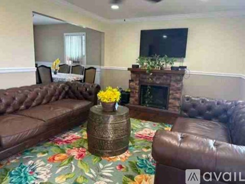 A living room with a brown leather couch, a coffee table with yellow flowers, and a fireplace with green plants on top.