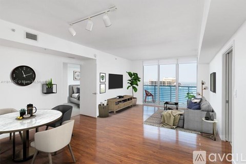 A living room with a white table and chairs, a couch, a TV, and a balcony with a view of the water.