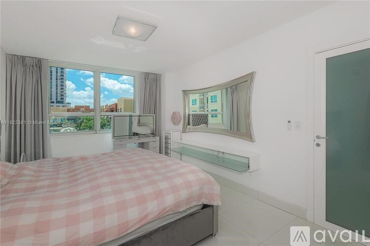 A bedroom with a bed, a mirror, and a window with a view of the city.