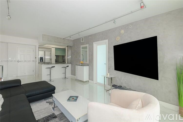 A modern living room with a black couch and a large flat screen TV mounted on the wall.