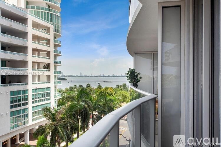 A modern building with a balcony overlooking a body of water and palm trees.