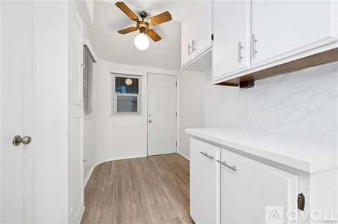 A white kitchen with a ceiling fan and wooden flooring.