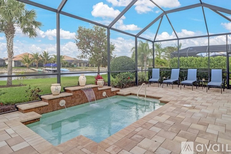 A pool surrounded by a glass wall with chairs and a table outside.
