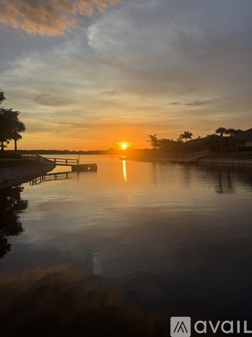 A serene sunset over a calm body of water with a dock and trees in the distance.
