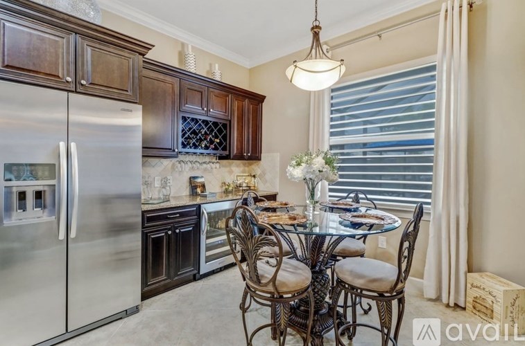 A kitchen with a glass table and chairs, a refrigerator, and a window with blinds.