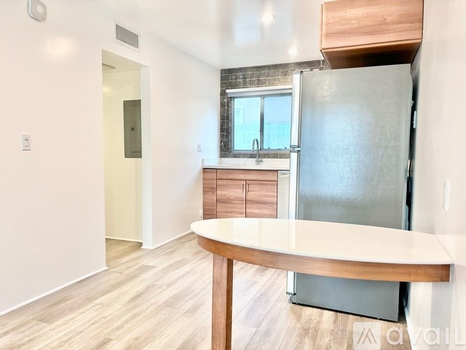 A kitchen with a refrigerator, table, and cabinets.