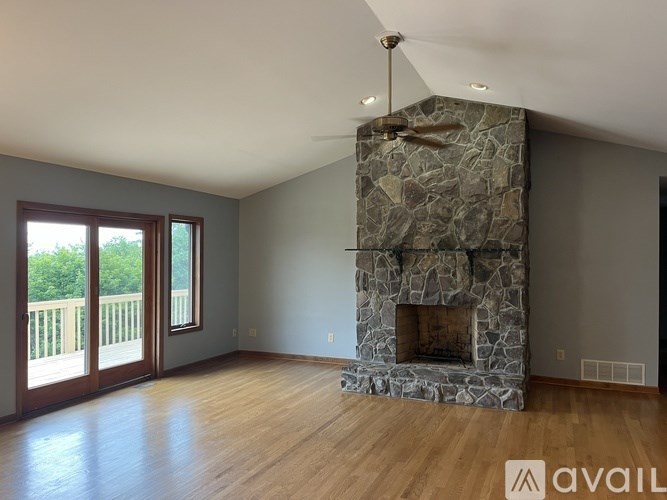 A stone fireplace in a room with wooden floors and a ceiling fan.