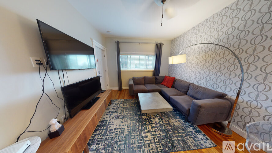 A living room with a grey couch, a flat screen TV on a wooden stand, a coffee table, and a patterned rug.