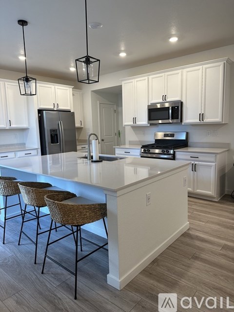 A kitchen with white cabinets and a white island with three barstools.