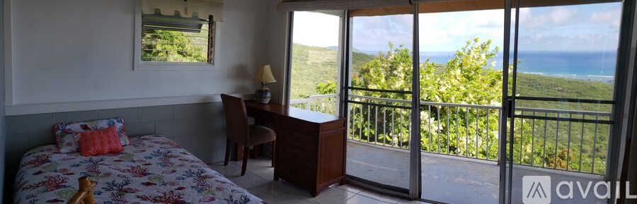 A bedroom with a large bed and a desk with a chair and a window overlooking the ocean.