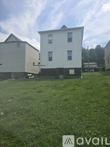 A grassy field with two white houses and a car parked in front of one.