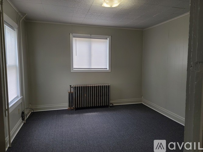 A room with a carpeted floor, a window with blinds, and a radiator.