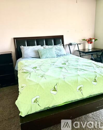 A bed with a green comforter and white pillows sits in a room with a black headboard.