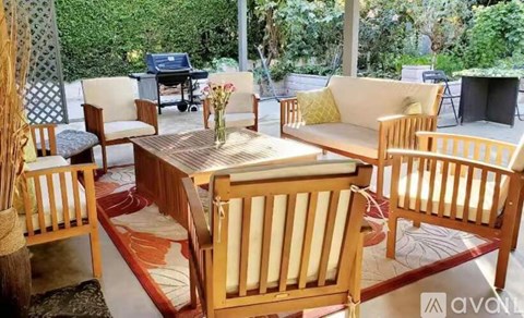 A wooden table with chairs and a sofa in a room with a view of greenery outside.