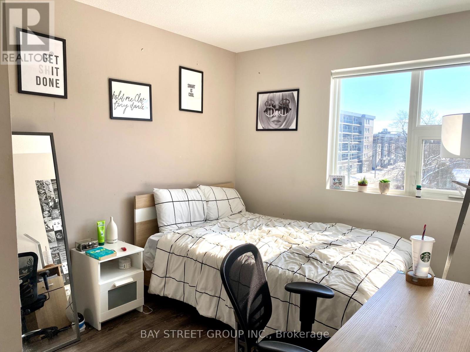 A bedroom with a bed, desk, chair, and a window overlooking a city.