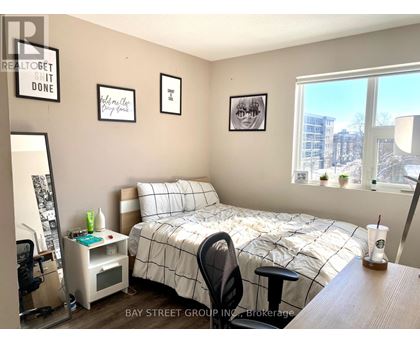 A bedroom with a bed, desk, chair, and a window overlooking a city.