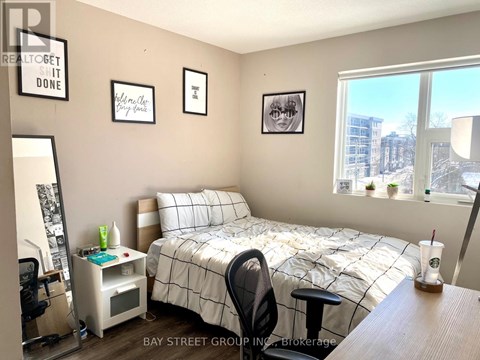 A bedroom with a bed, desk, chair, and a window overlooking a city.