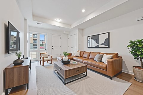 A living room with a brown couch, a coffee table, and a flat screen TV mounted on the wall.
