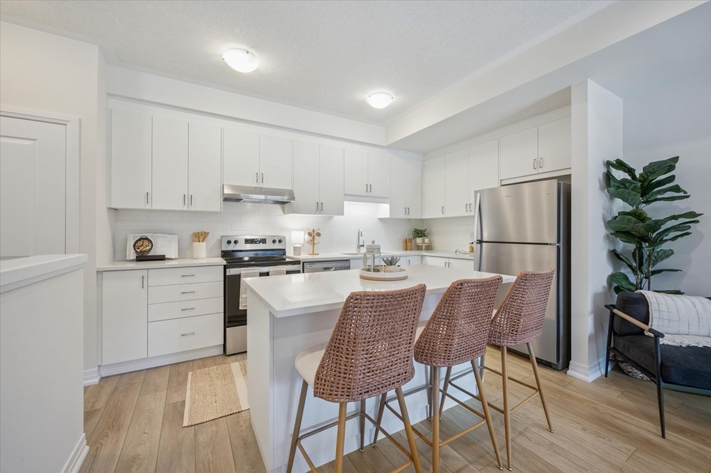A kitchen with white cabinets and a white island with two chairs.