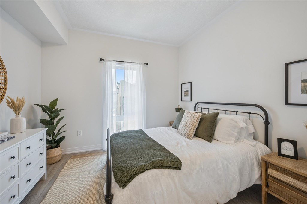 A bedroom with a bed, nightstand, and a plant.