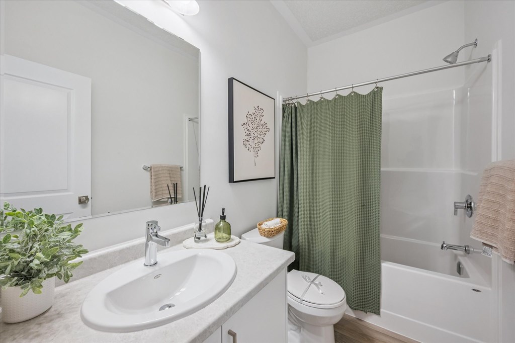 A white bathroom with a green shower curtain.