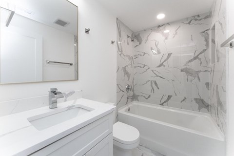 A white bathroom with a marble patterned shower.