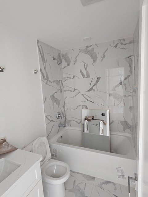 A white toilet sits next to a bathtub in a bathroom with marble wall tiles.