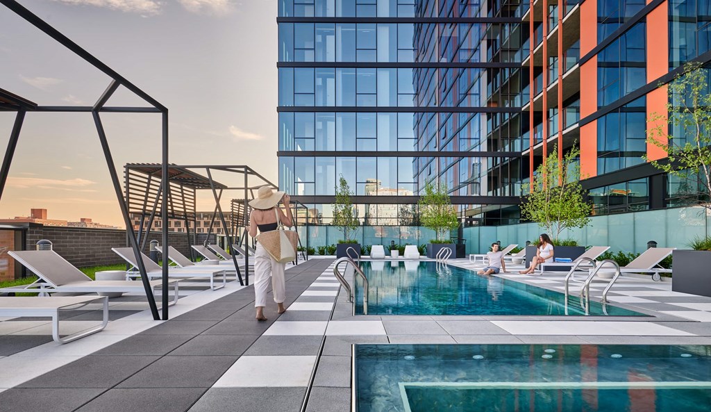 A modern outdoor pool area with people relaxing and a tall building in the background.