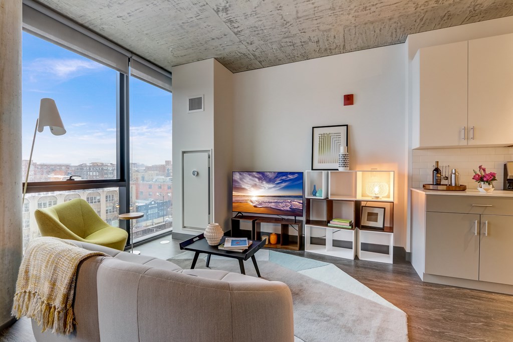 A living room with a couch, a chair, a table, a television, and a window with a view of the city.