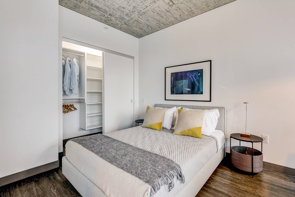 A bedroom with a bed, pillows, a basket, and a painting on the wall.