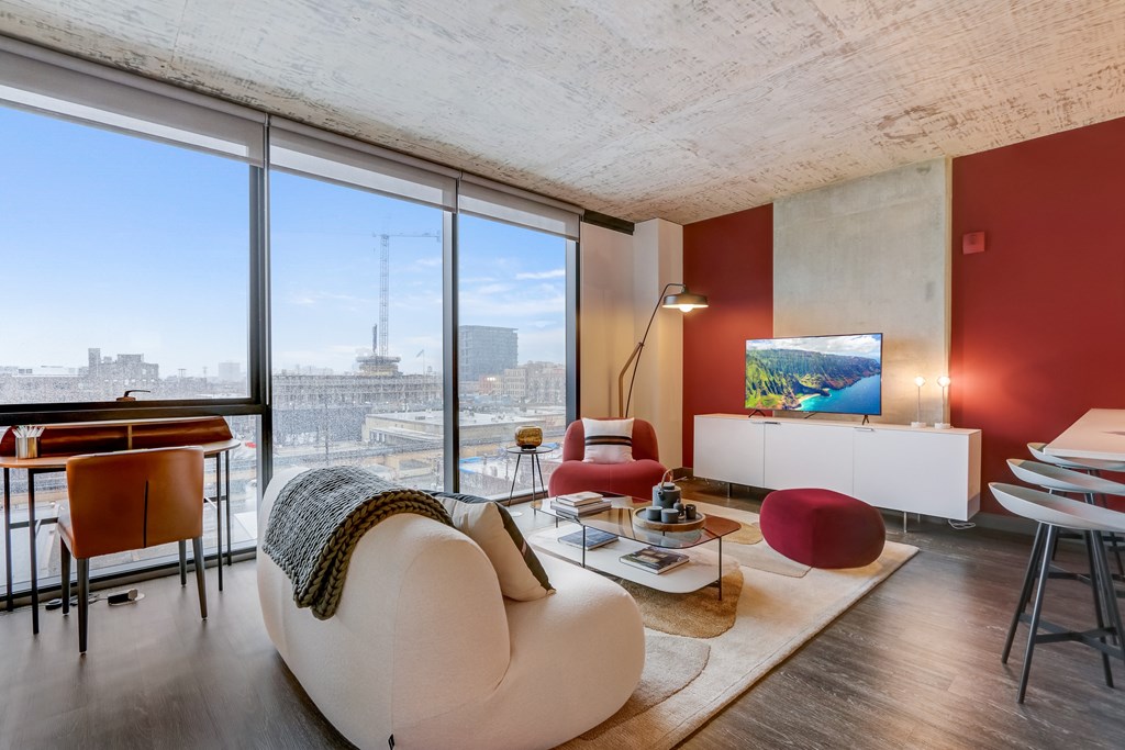 A living room with a white sofa and a large window overlooking a cityscape.