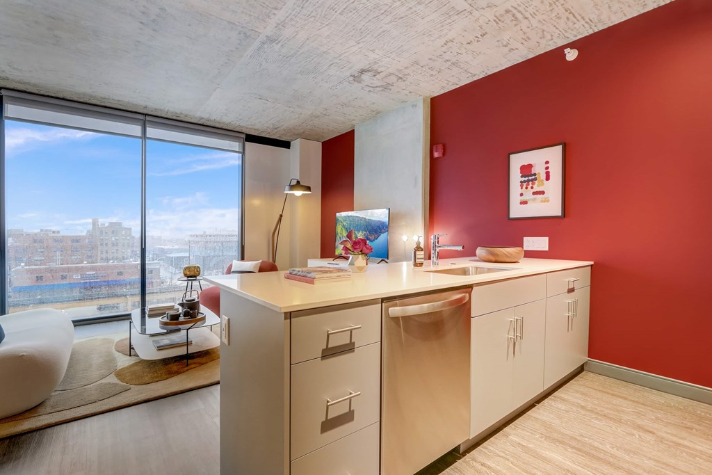 A modern kitchen with red walls and a large window overlooking the city.